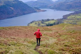 A man running down a hill with lake in the background